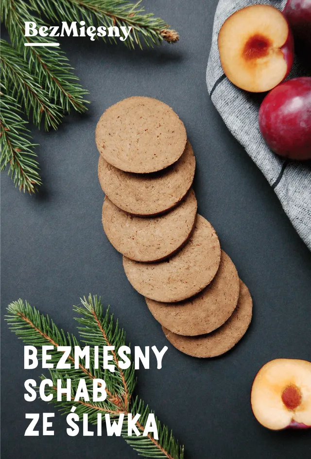 Packshot of Bezmięsny schab ze śliwką: plant-based pork loin slices with plum, fanned out on a dark background with fir sprigs and halved plums