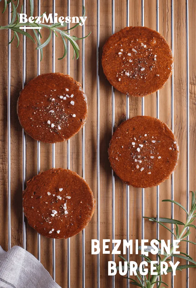 Packshot of Bezmięsne burgery: four plant-based burger patties topped with salt flakes on a grill rack with rosemary sprigs