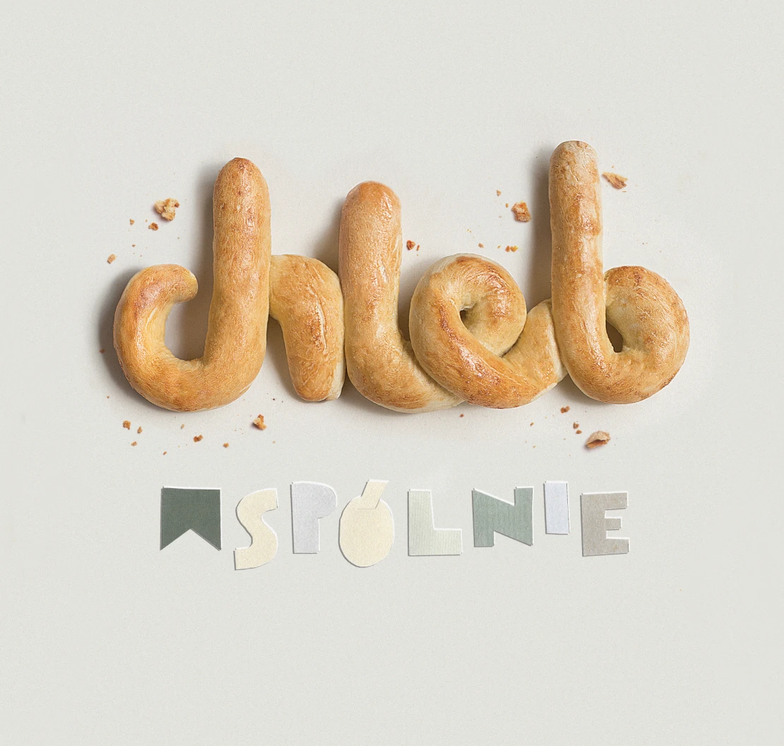 The words "chleb wspólnie" formed from baked bread dough and paper letters on a pale grey table