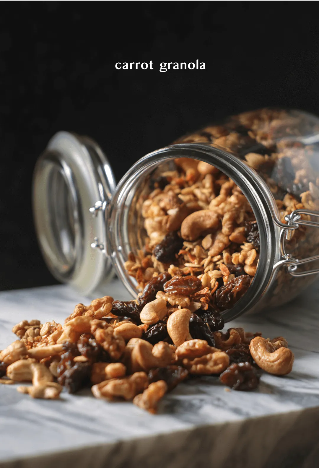 Jar of carrot granola tipped over on a marble ledge, spilling walnuts, cashews and raisins, titled "carrot granola"