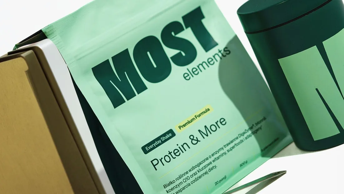 Mint-green MOST Elements Protein & More pouch leaning against a dark tin on a gold box